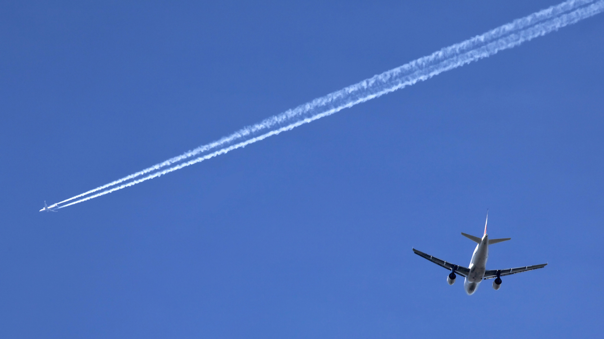 Two airplanes against clear blue sky with contrails