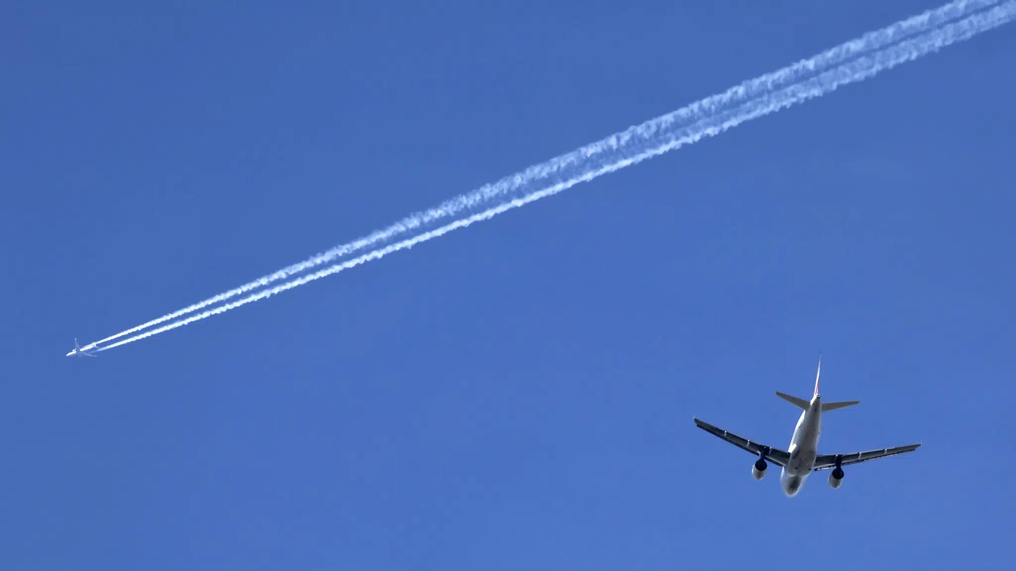 Two airplanes against clear blue sky with contrails