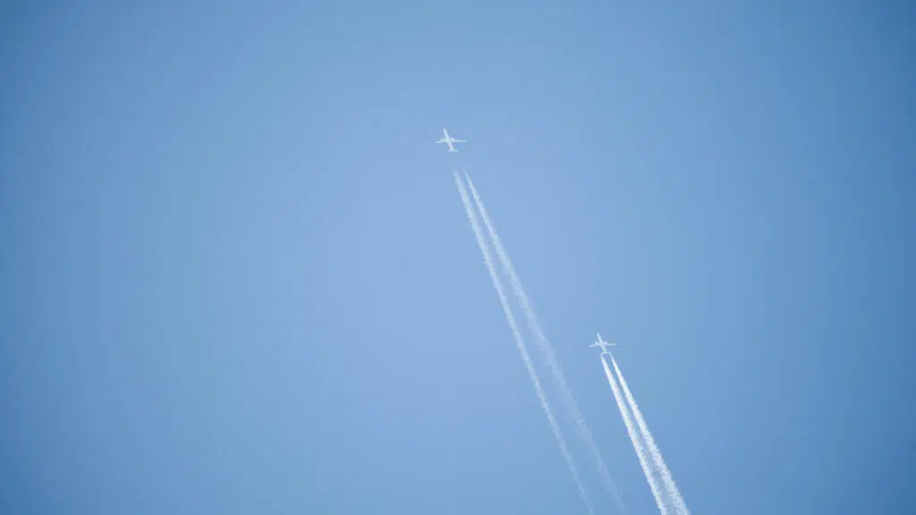 Two airplanes against clear blue sky with contrails