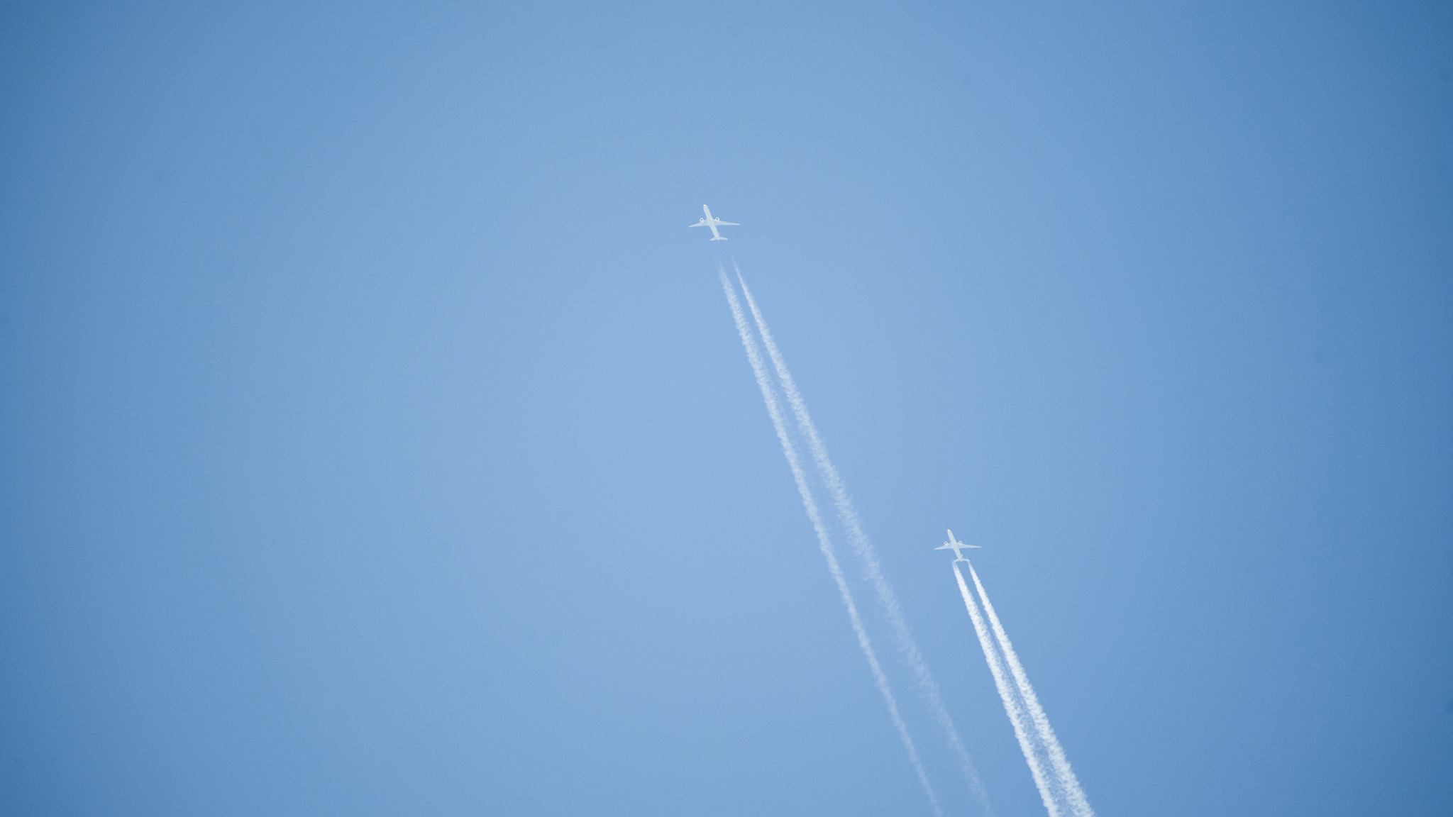 Two airplanes against clear blue sky with contrails