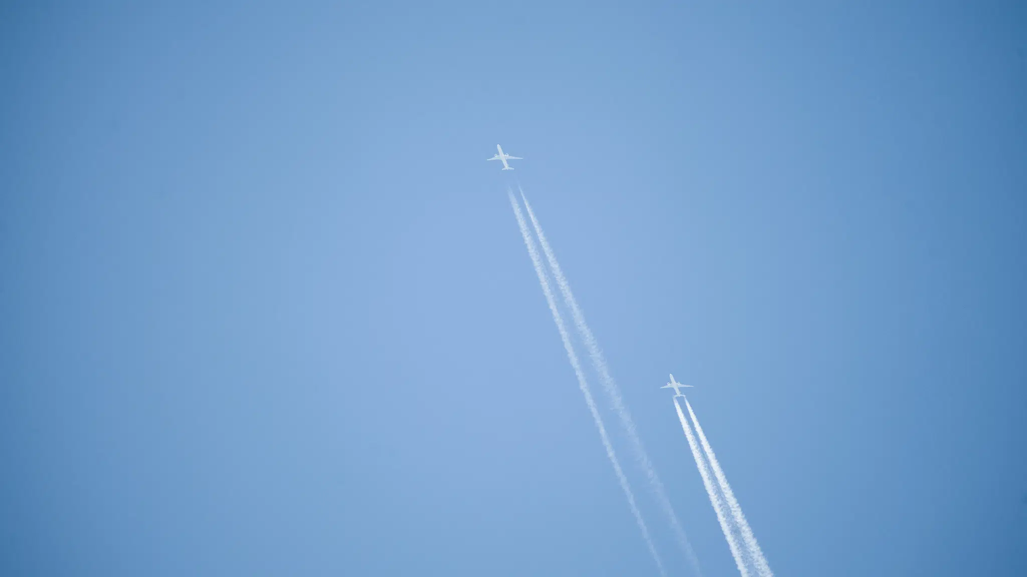 Two airplanes against clear blue sky with contrails